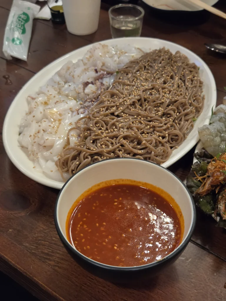 Thinly sliced squid over buckwheat noodles, with a separate bowl of red sauce.