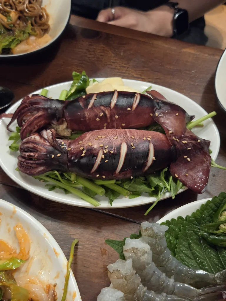 A whole steamed squid with cuts across its body, resting on leafy greens.